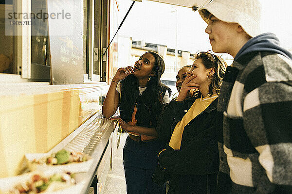 Männliche und weibliche Freunde wählen Essen aus der Speisekarte aus  während sie in der Nähe des Verkaufsstandes stehen