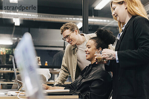 Lächelndes multirassisches Team  das über einem Laptop diskutiert  während es eine Strategie im Büro plant