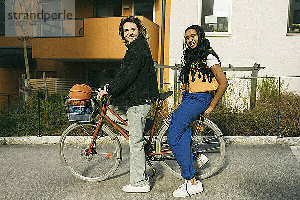 Porträt von lächelnden Freundinnen auf dem Fahrrad sitzend vor einem Gebäude am Fußweg