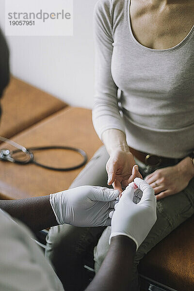 Arzt mit Handschuhen bei der Kontrolle des Blutzuckerspiegels einer Patientin in der Klinik