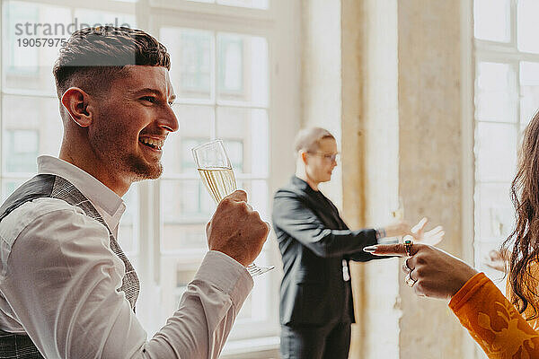 Seitenansicht eines lächelnden Geschäftsmanns  der während einer Veranstaltung im Kongresszentrum Weißwein trinkt