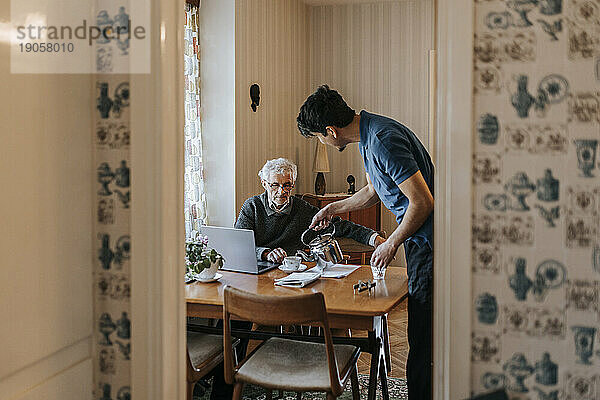 Seitenansicht einer männlichen Pflegekraft  die einem älteren Mann zu Hause Tee serviert