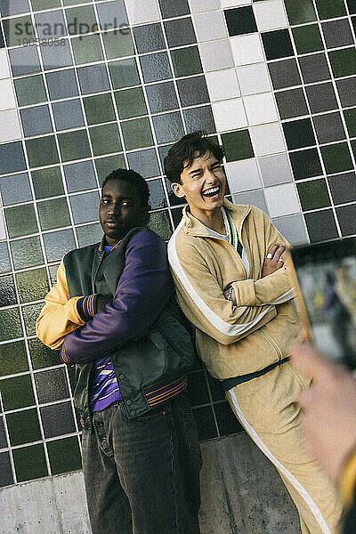 Junger Mann lacht  während er mit einem männlichen Freund an einer gekachelten Wand steht