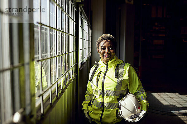 Porträt einer lächelnden jungen Arbeiterin  die in einer Fabrik am Fenster steht