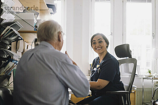 Zufriedene Krankenschwester  die einem älteren männlichen Patienten bei einem Besuch in der Klinik zuhört