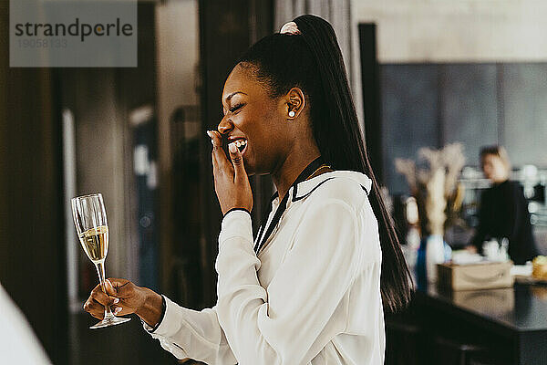 Seitenansicht einer glücklichen Geschäftsfrau  die lacht und ein Glas während einer Veranstaltung im Kongresszentrum hält