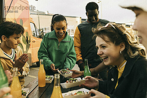 Glückliche männliche und weibliche Freunde genießen Snacks mit Getränken in der Nähe von Food Truck
