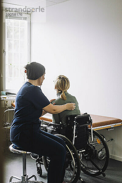 Seitenansicht einer Krankenschwester  die eine im Rollstuhl sitzende Frau in einer Klinik untersucht