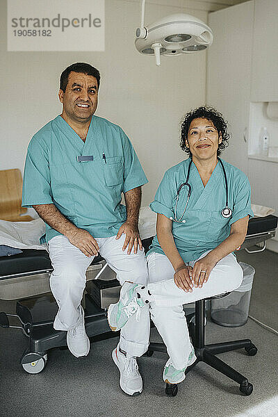 Porträt eines lächelnden Arztes und einer lächelnden Ärztin  die im Krankenhaus sitzen