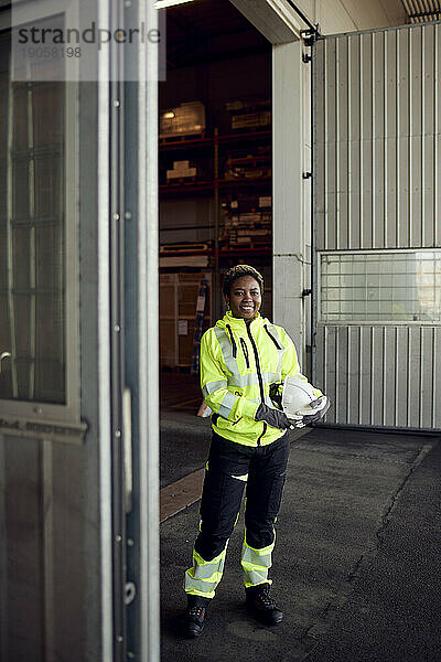 Porträt einer lächelnden jungen Arbeiterin in Arbeitskleidung  die in einer Fabrik steht