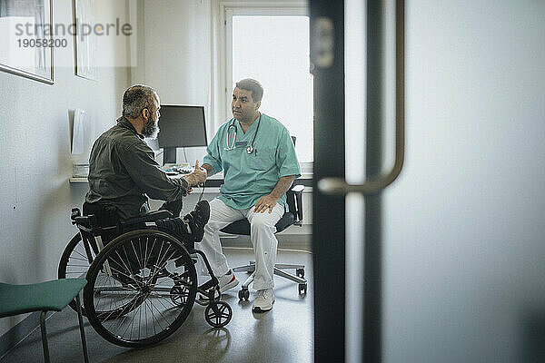 Arzt im Gespräch mit einem männlichen Patienten im Rollstuhl im Krankenhaus