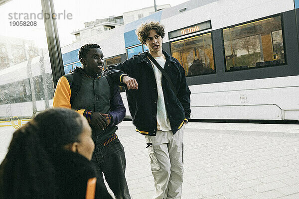 Jugendlicher diskutiert mit männlichem Freund beim Warten am Bahnhof