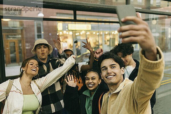 Glücklicher Mann nimmt Selfie mit fröhlichen Freunden durch Smartphone am Bahnhof