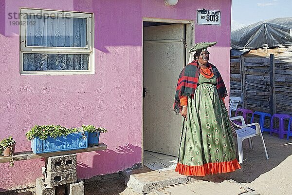 Hererofrau in traditioneller farbenfroher Kleidung vor ihrem Haus in einem Township bei Swakopmund  Namibia  Südafrika  Afrika