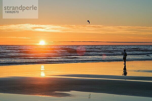 Sonnenuntergang über dem Atlantik mit der Silhouette eines Fotografen  der am Strand von Fonte da Telha  an der Costa da Caparica  Portugal  Bilder von der Brandung macht  Europa