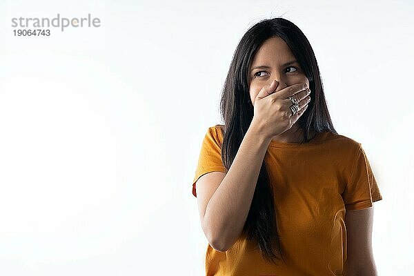 Nahaufnahme einer attraktiven jungen lateinamerikanischen Frau  die ihren Mund bedeckt und schelmisch zur Seite schaut. Studio Porträt auf weißem Hintergrund