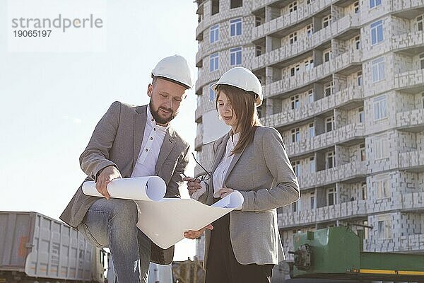 Zwei Architekten  die einen Bauplan in der Hand halten und ein Projekt besprechen  während sie zusammenarbeiten