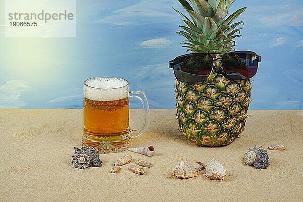 Natürliche Ananas mit Sonnenbrille auf dem Sand des Strandes mit einem Bierkrug mit Schaum