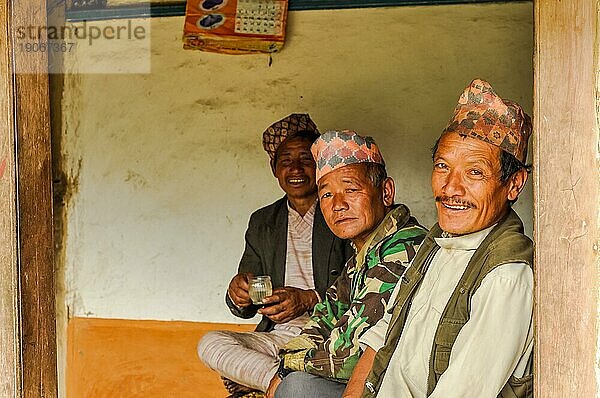 Kanchenjunga Trek  Nepal  etwa im Mai 2012: Drei Männer mit Mützen auf dem Kopf sitzen auf einer Bank und lächeln in die Kamera in Kanchenjunga Trek  Nepal. Dokumentarischer Leitartikel  Asien