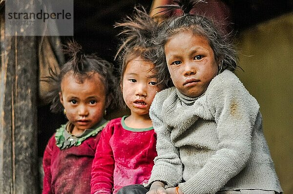 Dolpo  Nepal  ca. Mai 2012: Drei junge Mädchen mit braunen Haaren und braunen Augen sitzen auf einer Bank und schauen traurig in die Fotokamera in Dolpo  Nepal. Dokumentarischer Leitartikel  Asien