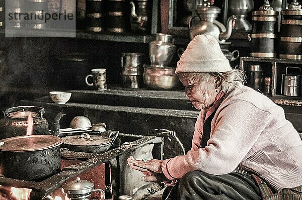 Kanchenjunga Trek  Nepal  ca. Mai 2012: Alte Frau mit weißer Mütze kniet in der Nähe des Ofens und blickt auf ihren Ring im Kanchenjunga Trek  Nepal. Dokumentarischer Leitartikel  Asien