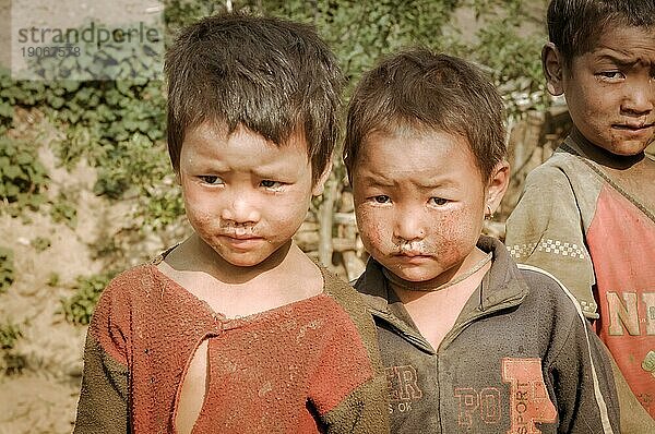 Dolpo  Nepal  etwa im Mai 2012: Ein braunhaariges Mädchen und zwei Jungen posieren mit Schmutz im Gesicht und auf der Kleidung in Dolpo  und runzeln die Stirn in Richtung Fotokamera. Dokumentarischer Leitartikel  Asien