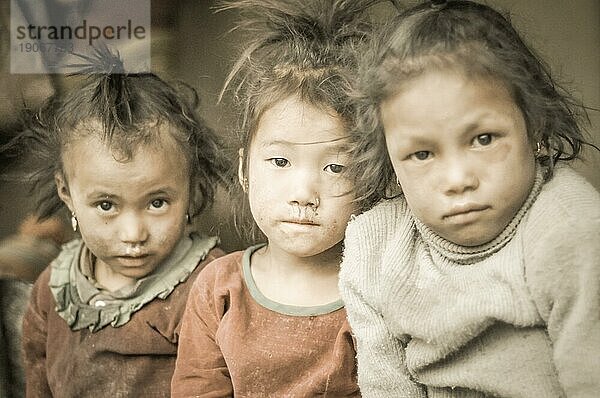 Dolpo  Nepal  ca. Mai 2012: Drei junge Mädchen mit braunen Haaren und braunen Augen sitzen auf einer Bank und schauen traurig in die Fotokamera in Dolpo  Nepal. Dokumentarischer Leitartikel  Asien