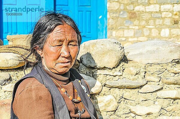 Dolpo  Nepal  ca. Juni 2012: Alte Frau mit Falten in braunem Hemd und schwarzer Weste trägt eine orangefarbene Halskette und blickt nach unten in Dolpo  Nepal. Dokumentarischer Leitartikel  Asien