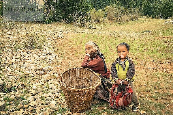 Dolpo  Nepal  ca. Juni 2012: Alte grauhaarige Frau kniet neben einem Korb und einem kleinen Kind in gelbem Hemd mit roter Tasche in den Händen und sie schauen in die Kamera in Dolpo  Nepal. Dokumentarischer Leitartikel  Asien