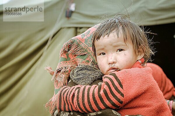 Dolpo  Nepal  ca. Juni 2012: Kleines braunhaariges Mädchen in schwarz rot gestreiftem Hemd umarmt ihre Mutter und schaut mit braunen Augen traurig in die Kamera in Dolpo  Nepal. Dokumentarischer Leitartikel  Asien