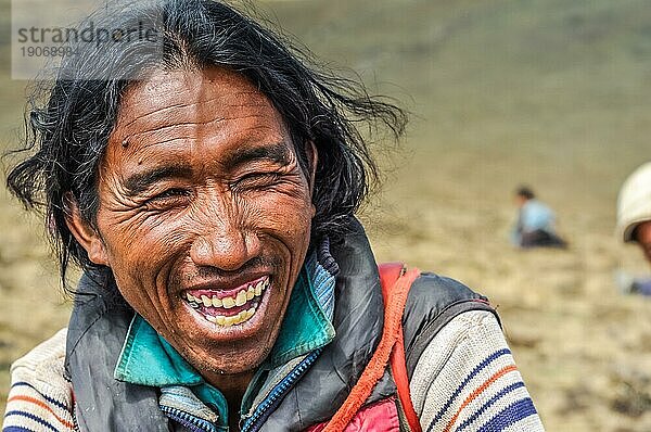 Dolpo  Nepal  ca. Juni 2012: Einheimischer schwarzhaariger Mann in Jacke sitzt auf dem Boden und lacht fröhlich in Dolpo  Nepal. Dokumentarischer Leitartikel  Asien