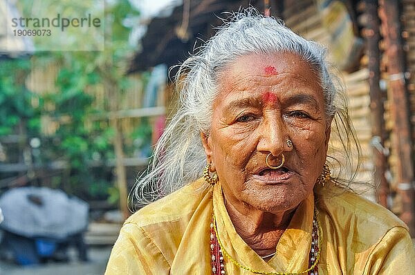 Damak  Nepal  ca. Mai 2012: Alte Frau mit roten Punkten auf der Stirn und goldenem Piercing in der Nase posiert in gelbem Hemd im nepalesischen Flüchtlingslager in Damak  Nepal. Dokumentarischer Leitartikel  Asien