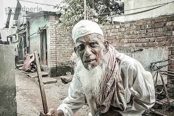 Khulna  Bangladesch  ca. Juli 2012: Alter Mann in weißer Kleidung und weißer Mütze mit langem weißen Bart hält einen Holzstock im Slum in Khula  Bangladesch. Dokumentarischer Leitartikel  Asien