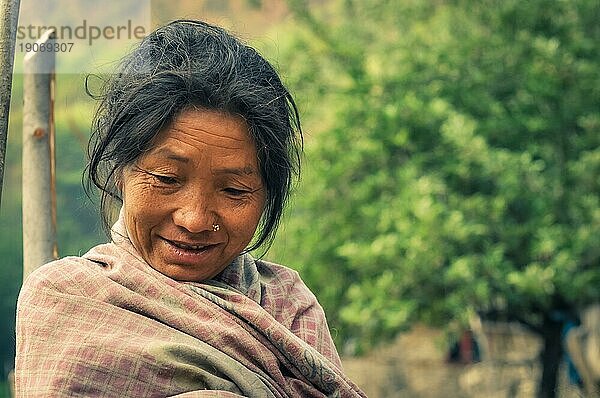 Dolpo  Nepal  etwa im Mai 2012: Sanft lächelnde einheimische Frau mit Nasenpiercing blickt nach unten und deckt sich mit einer karierten Decke in Dolpo  zu. Dokumentarischer Leitartikel  Asien