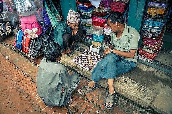 Bhaktapur  Nepal  ca. Juni 2012: Drei einheimische Männer sitzen auf dem Boden vor einem Geschäft und spielen Schach in Bhaktapur  Nepal. Dokumentarischer Leitartikel  Asien