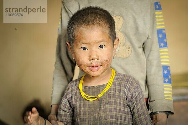 Dolpo  Nepal  ca. Mai 2012: Kleines braunäugiges Mädchen in kariertem Hemd trägt gelbe Perlen und schaut freundlich in die Kamera in Dolpo  Nepal. Dokumentarischer Leitartikel  Asien