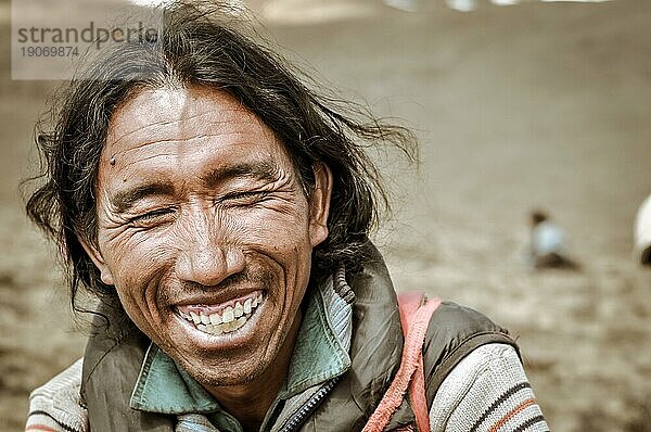 Dolpo  Nepal  ca. Juni 2012: Einheimischer schwarzhaariger Mann in Jacke sitzt auf dem Boden und lacht fröhlich mit geschlossenen Augen in Dolpo  Nepal. Dokumentarischer Leitartikel  Asien
