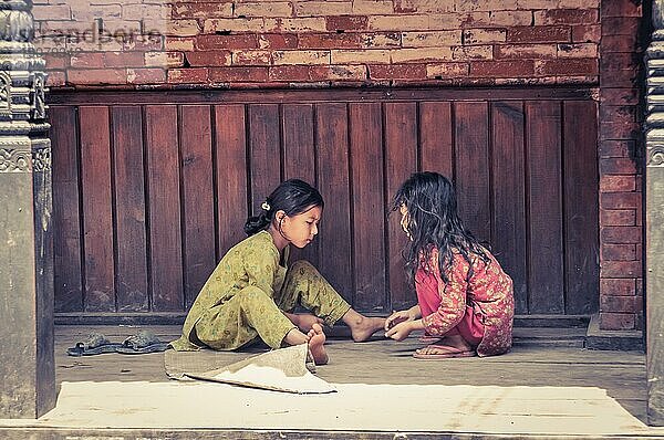 Bhaktapur  Nepal  ca. Juni 2012: Zwei junge Mädchen mit langen schwarzen Haaren sitzen draußen auf dem Boden und spielen Spiele in Bhaktapur  Nepal. Dokumentarischer Leitartikel  Asien