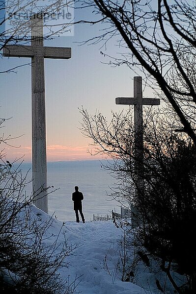Ein Mensch steht unter den Gipfelkreuzen und schaut beim Sonnenuntergang ins nebelbedeckte Tal