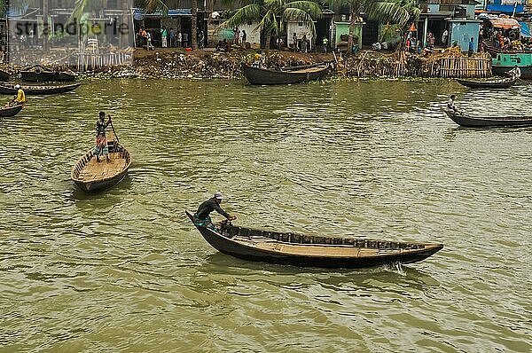 Dhaka  Bangladesch  ca. Juli 2012: Foto von einheimischen Männern in Booten auf dem Fluss im Hintergrund mit Menschen und Häusern am Ufer in Dhaka  Bangladesch. Dokumentarischer Leitartikel  Asien
