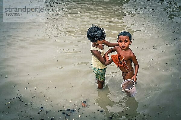 Sunderban  Bangladesch  ca. Juli 2012: Kleine einheimische Kinder waschen sich im Fluss  ein Junge hält einen Eimer und schaut stirnrunzelnd in die Kamera in Sunderban  Bangladesch. Dokumentarischer Leitartikel  Asien