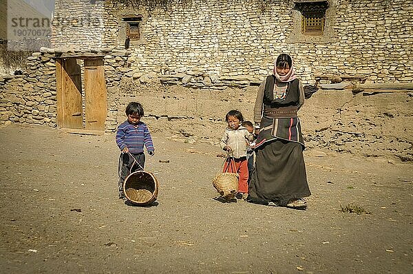 Dolpo  Nepal  ca. Juni 2012: Einheimische Frau in braunem Kleid mit Kopftuch mit ihren zwei kleinen Kindern mit kleinen Körben in Dolpo  Nepal. Dokumentarischer Leitartikel  Asien