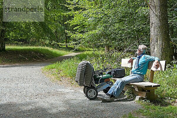 Behinderter sitzt auf einer Bank im Wald und genießt die Sonne