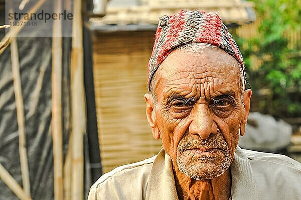Damak  Nepal  ca. Mai 2012: Alter Mann mit faltigem Gesicht und Mütze auf dem Kopf runzelt die Stirn und schaut traurig in die Kamera im nepalesischen Flüchtlingslager in Damak  Nepal. Dokumentarischer Leitartikel  Asien