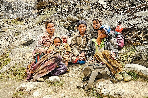 Dolpo  Nepal  ca. Juni 2012: Braunhaarige einheimische Frau sitzt mit ihren Kindern mit Jacken auf einem Stein und sie posieren für die Fotokamera in den schönen Bergen von Dolpo  Nepal. Dokumentarischer Leitartikel  Asien