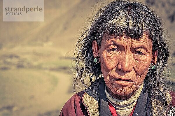 Dolpo  Nepal  ca. Juni 2012: Alte grauhaarige Frau mit faltigem Gesicht trägt blaue Ohrringe und schaut traurig in die Kamera in Dolpo  Nepal. Dokumentarischer Leitartikel  Asien
