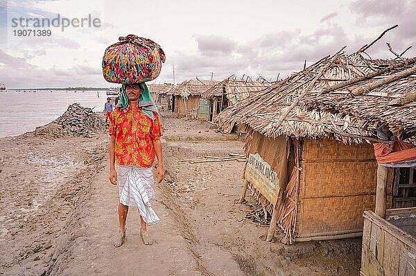 Sunderban  Bangladesch  ca. Juli 2012: Einheimischer Mann mit Schnurrbart steht im Schlamm in der Nähe eines Hauses mit einer schweren Last in einem bunten Tuch auf dem Kopf in Sunderban  Bangladesch. Dokumentarischer Leitartikel  Asien