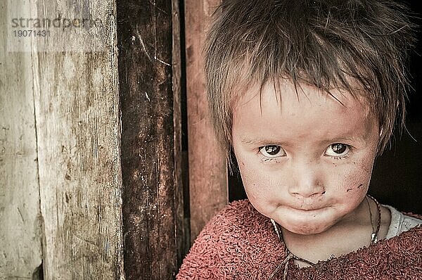 Dolpo  Nepal  ca. Mai 2012: Kleines Mädchen mit braunen  glitzernden Augen  bekleidet mit einem roten Pullover  schaut neugierig in die Kamera in Dolpo  Nepal. Dokumentarischer Leitartikel  Asien