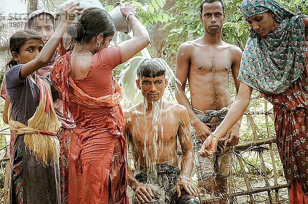 Paigacha  Bangladesch  ca. Juli 2012: Junge Mädchen in bunten Kleidern gießen Wasser auf einen sitzenden Jungen in Paigacha  Bangladesch. Dokumentarischer Leitartikel  Asien