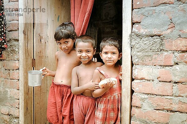 Khulna  Bangladesch  etwa im Juli 2012: Drei kleine Kinder in roter Kleidung stehen auf der Türschwelle und schauen neugierig in die Fotokamera in einem Slum in Khula  Bangladesch. Dokumentarischer Leitartikel  Asien